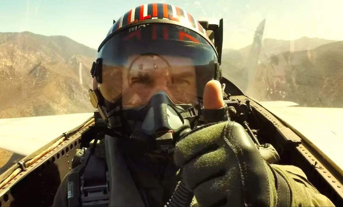 Tom Cruise in flight gear giving the camera a thumbs up from a fighter cockpit